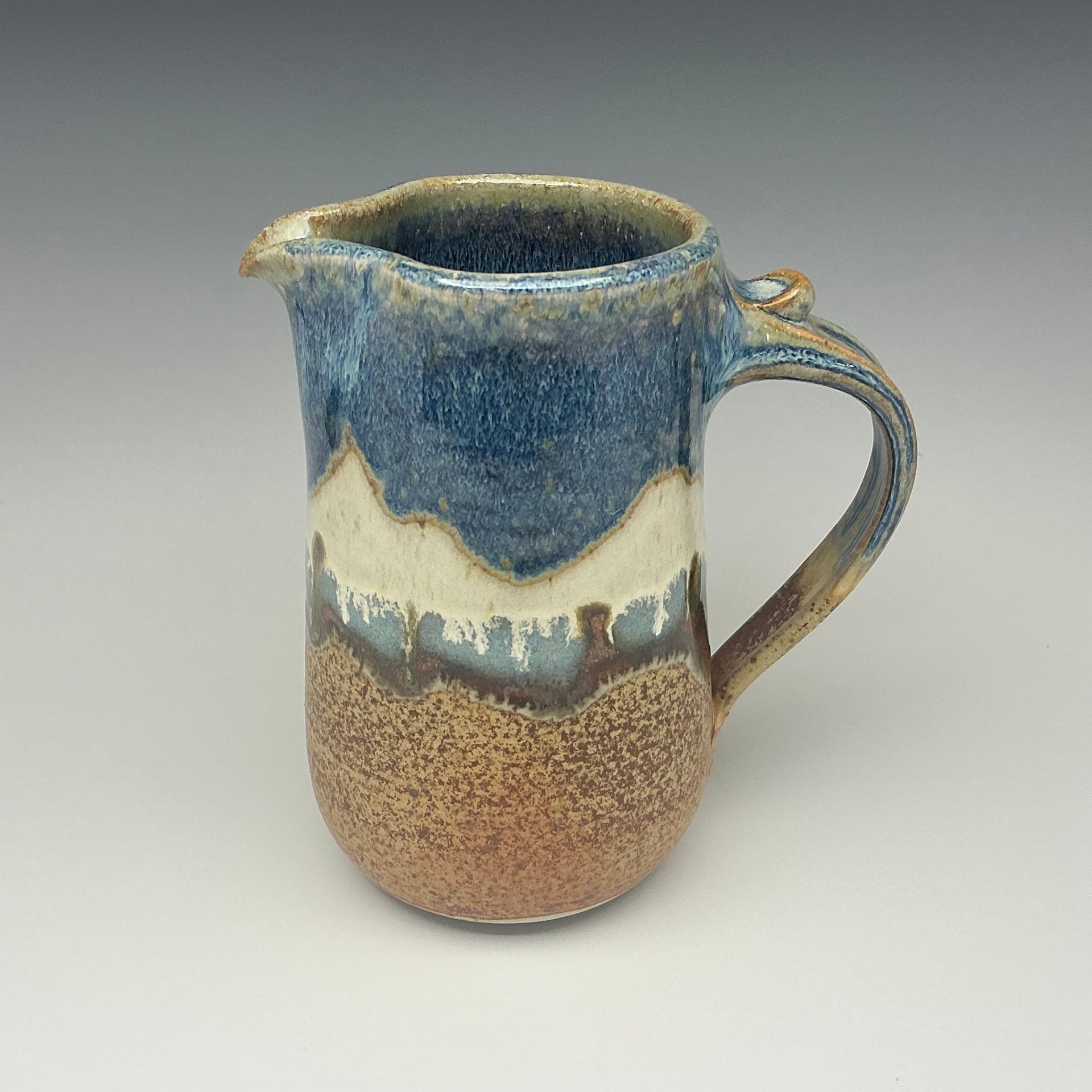 Ceramic pitcher with blue and brown glaze on a gray background