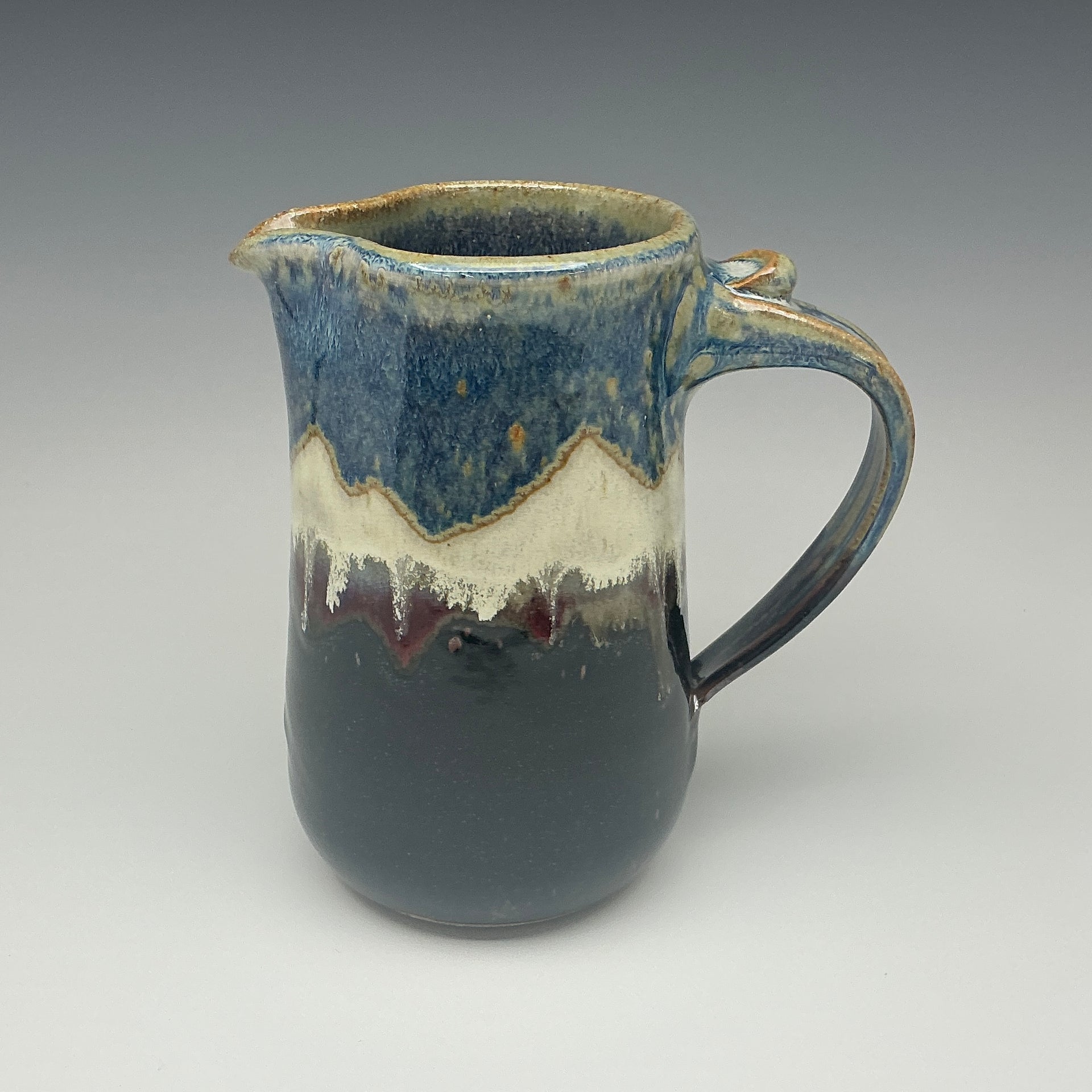 Ceramic pitcher with blue and brown glaze and an image of a mountain on it