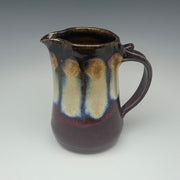 Ceramic pitcher with brown and red glaze on a gray background