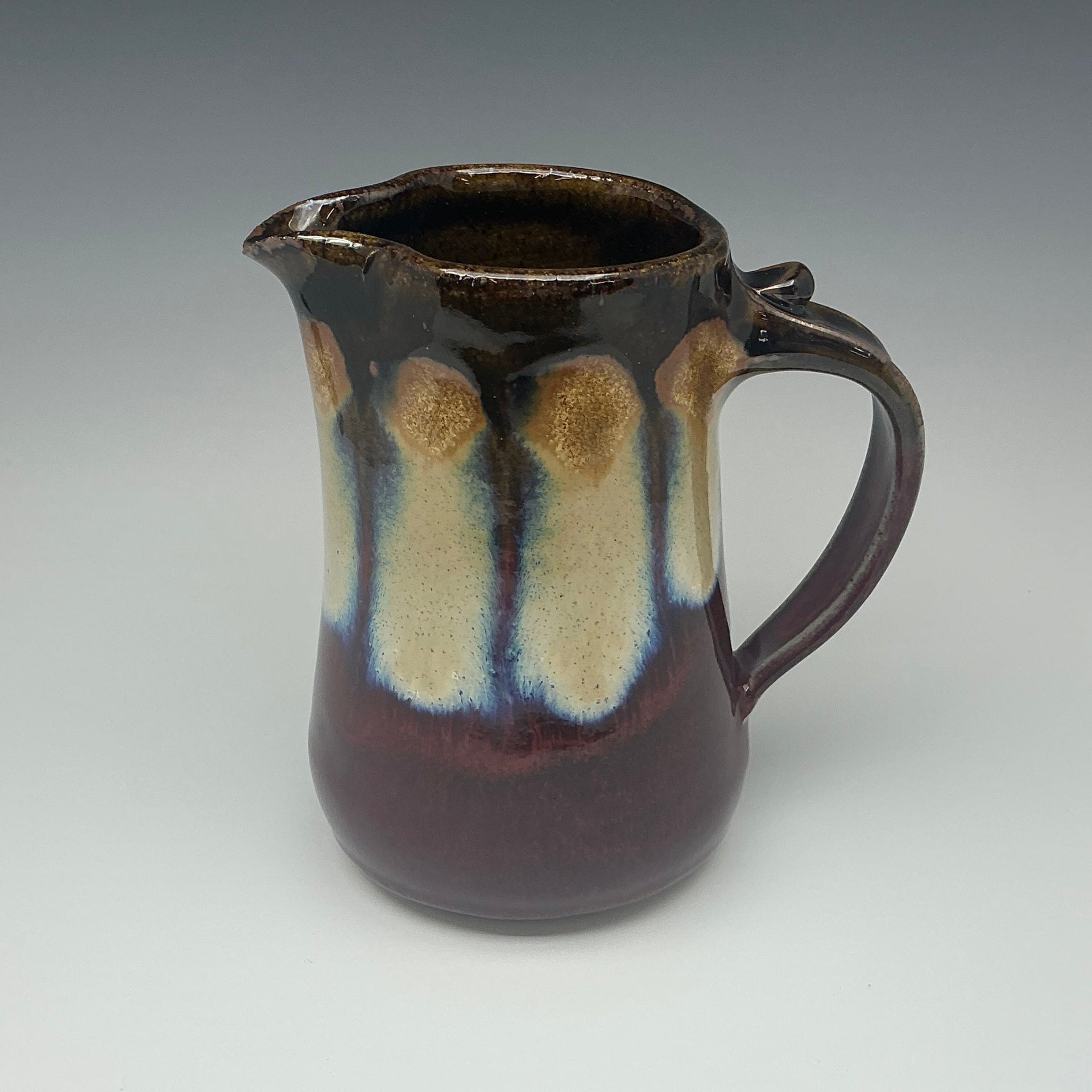 Ceramic pitcher with brown and red glaze on a gray background
