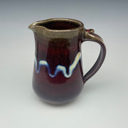 Ceramic pitcher in dark red with a wavy design on a gray background