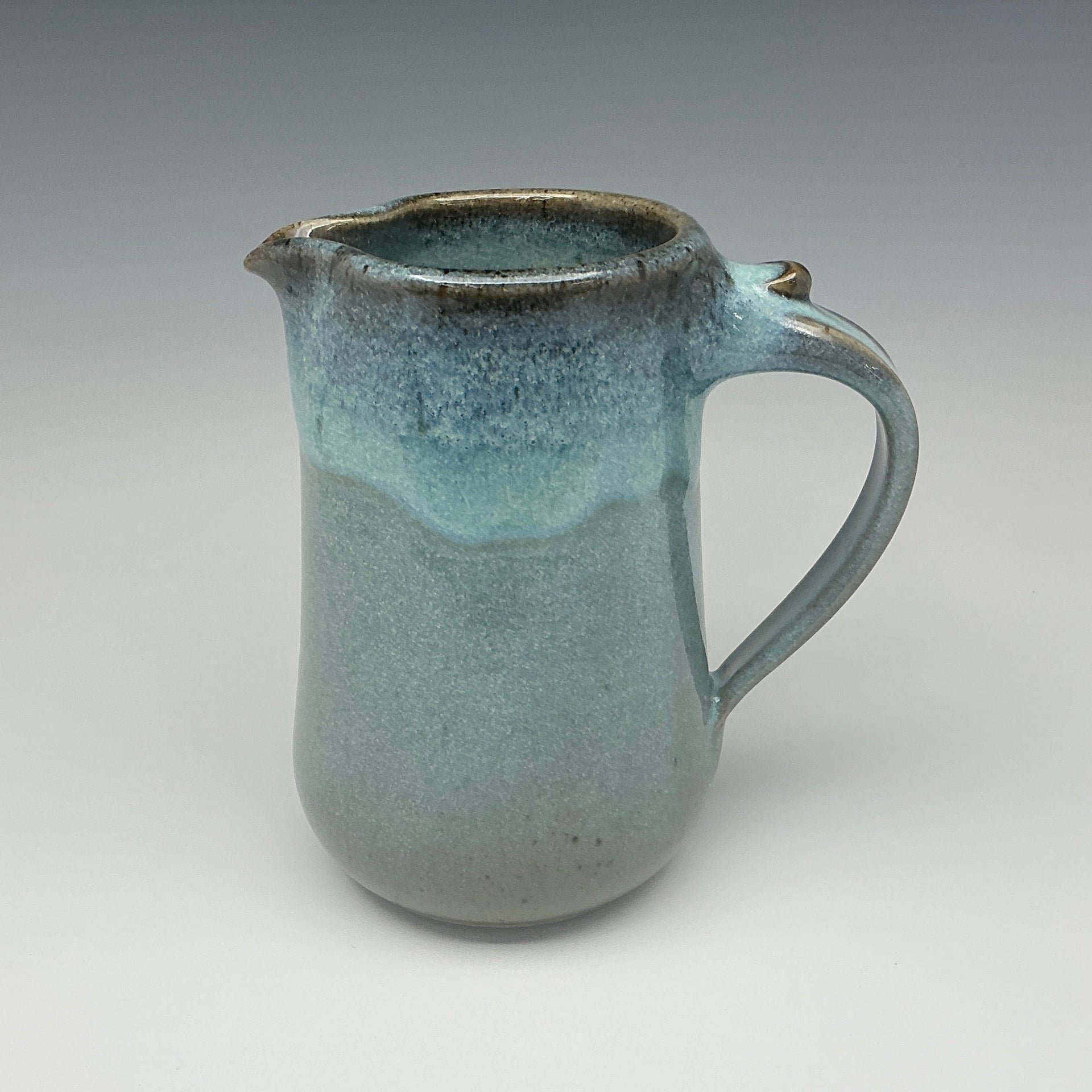 Teal ceramic pitcher on a gray background