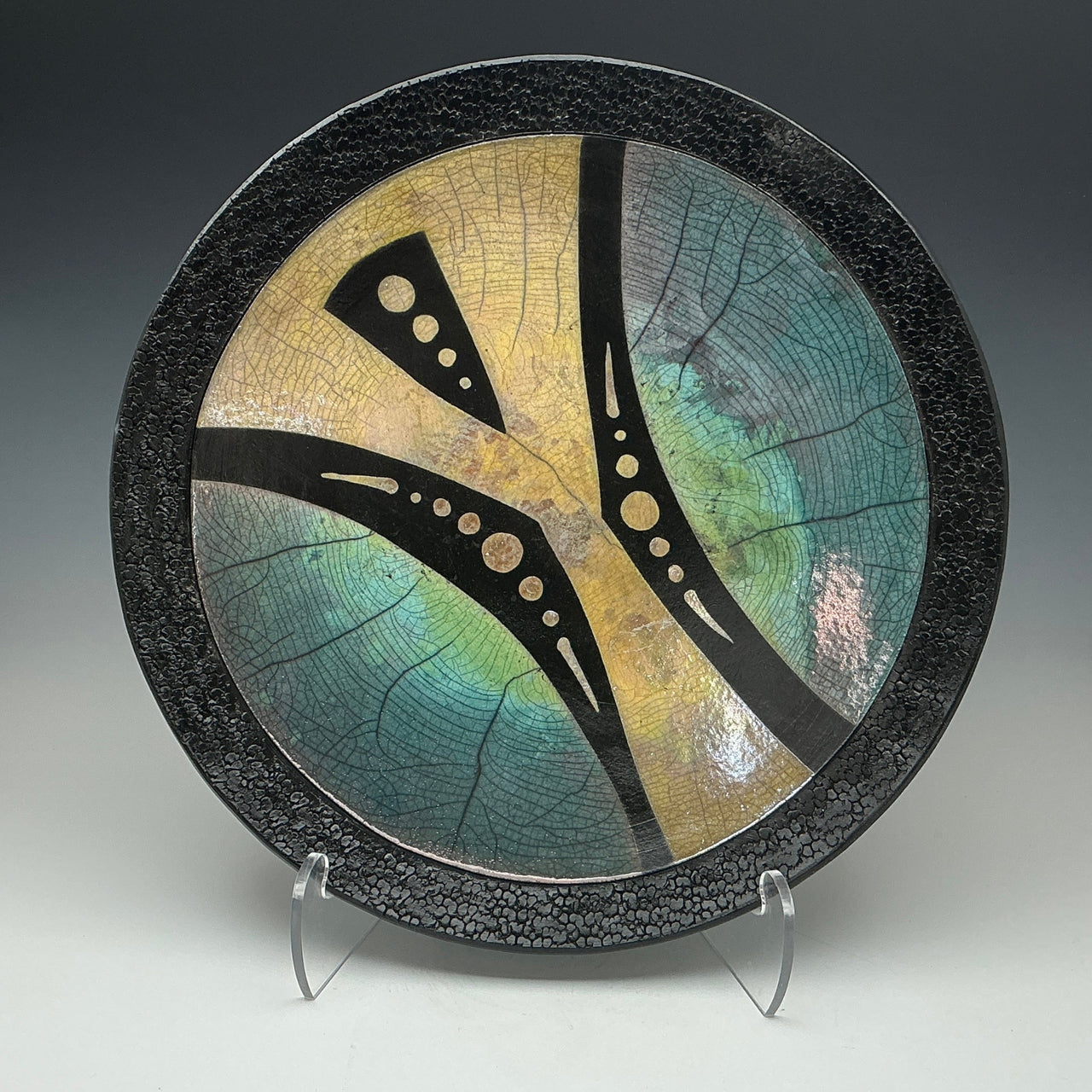 a Raku wall plate with an abstract image in gold teal and black