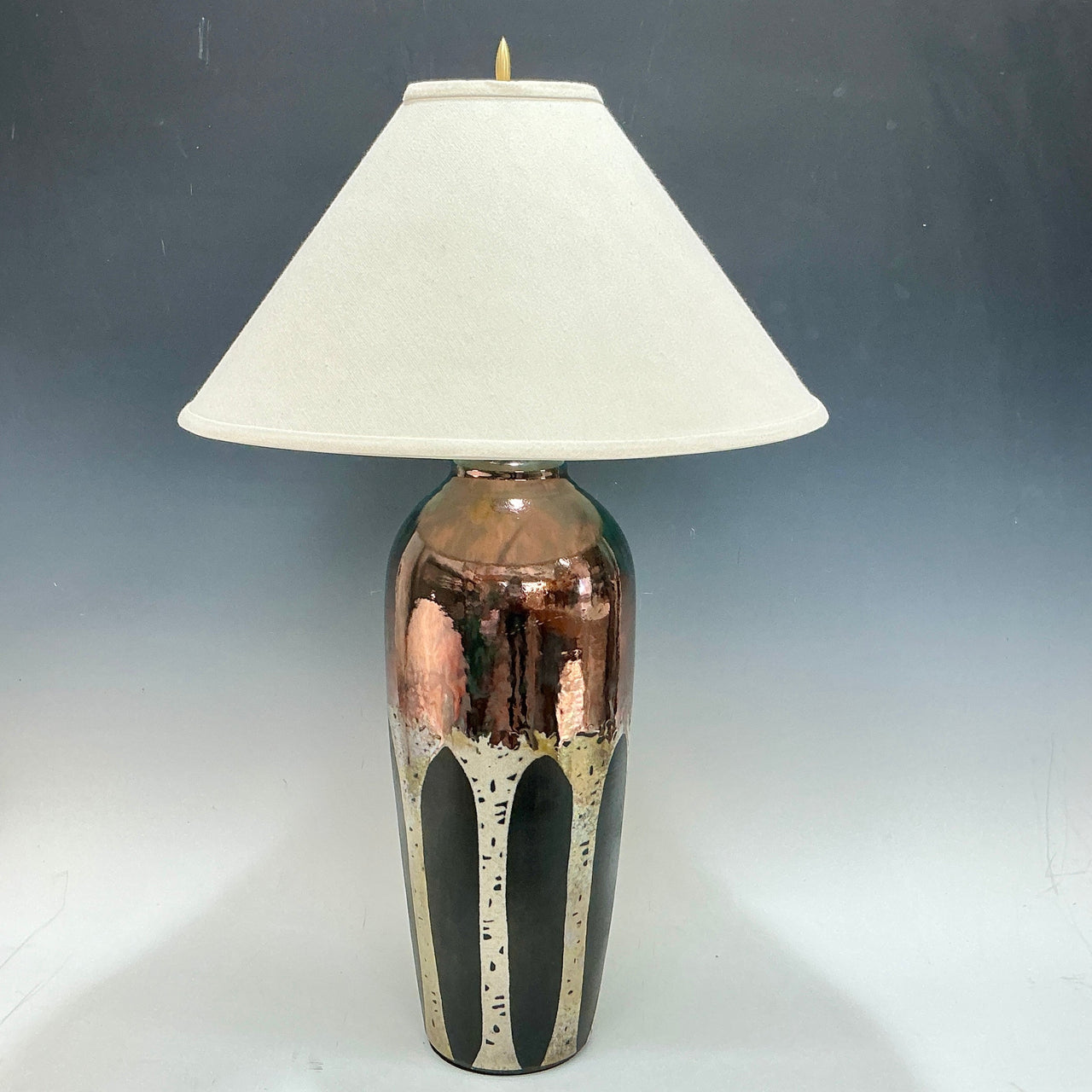 Table lamp with a decorative ceramic base of aspen trees on it and white shade on a gray background