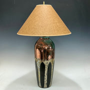 Table lamp with a decorative aspen trees in metalic colors and beige lampshade on a dark background