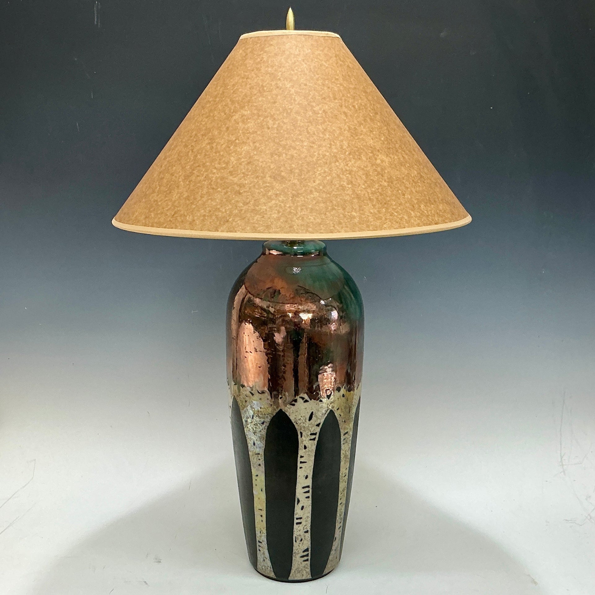 Table lamp with a decorative aspen trees in metalic colors and beige lampshade on a dark background