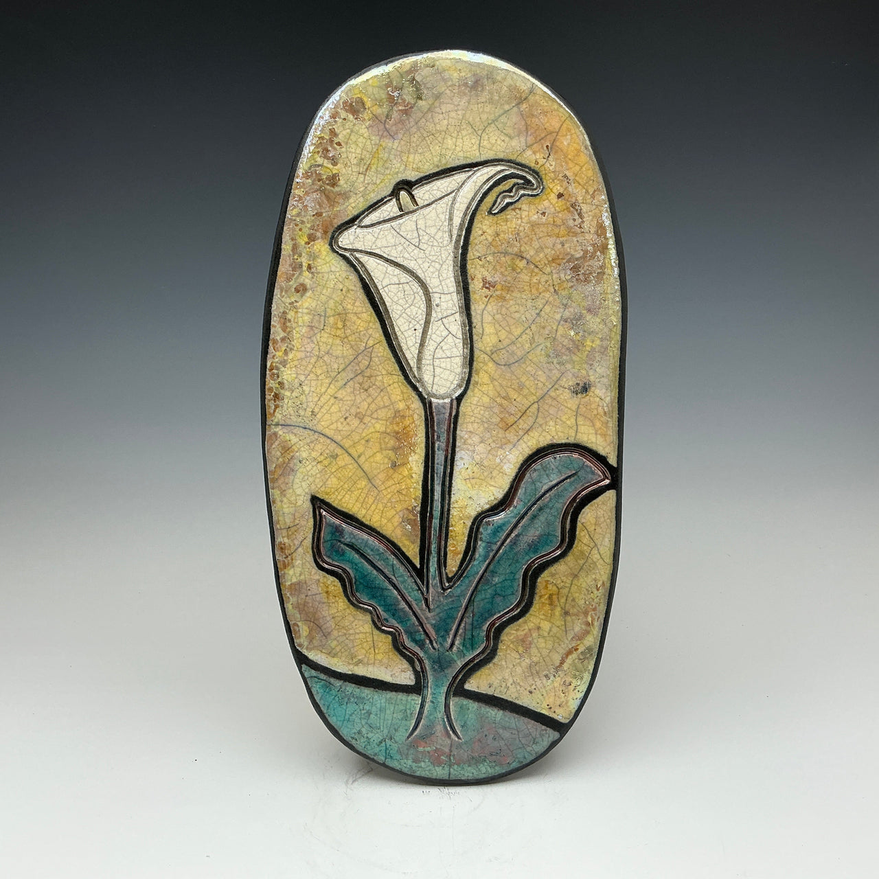 a Raku wall tile with an image of a calla Lilly on a gold background on it