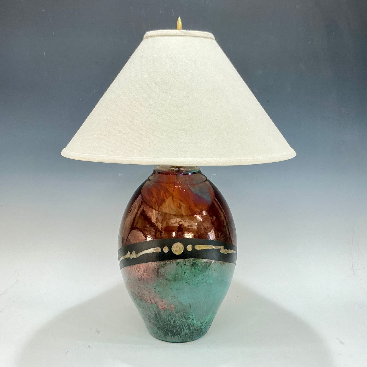 Decorative table lamp with a copper and teal base and white shade on a gradient background