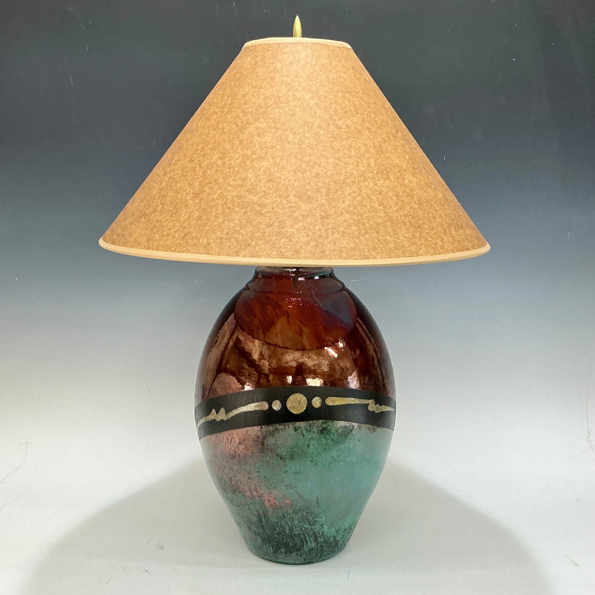 Decorative lamp with a brown and green base and a beige lampshade on a gray background