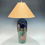 Decorative lamp with a dark blue base and gold accents, featuring a beige lampshade on a gray background.
