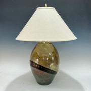Decorative lamp with a textured gold and teal base and white shade on a gradient background
