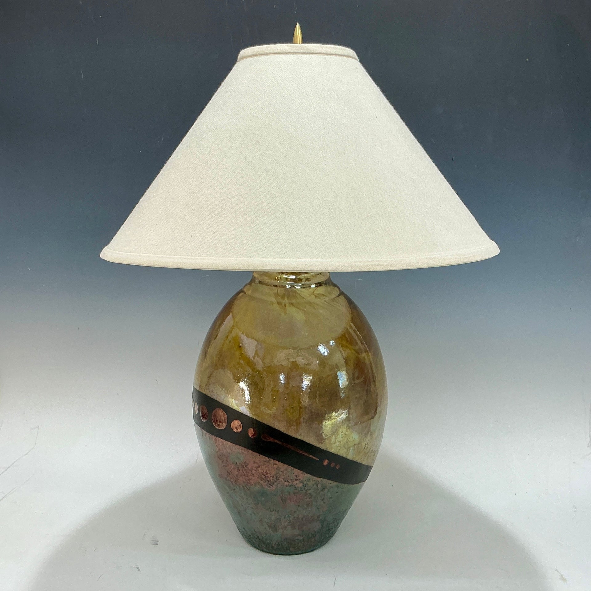 Decorative lamp with a textured gold and teal base and white shade on a gradient background