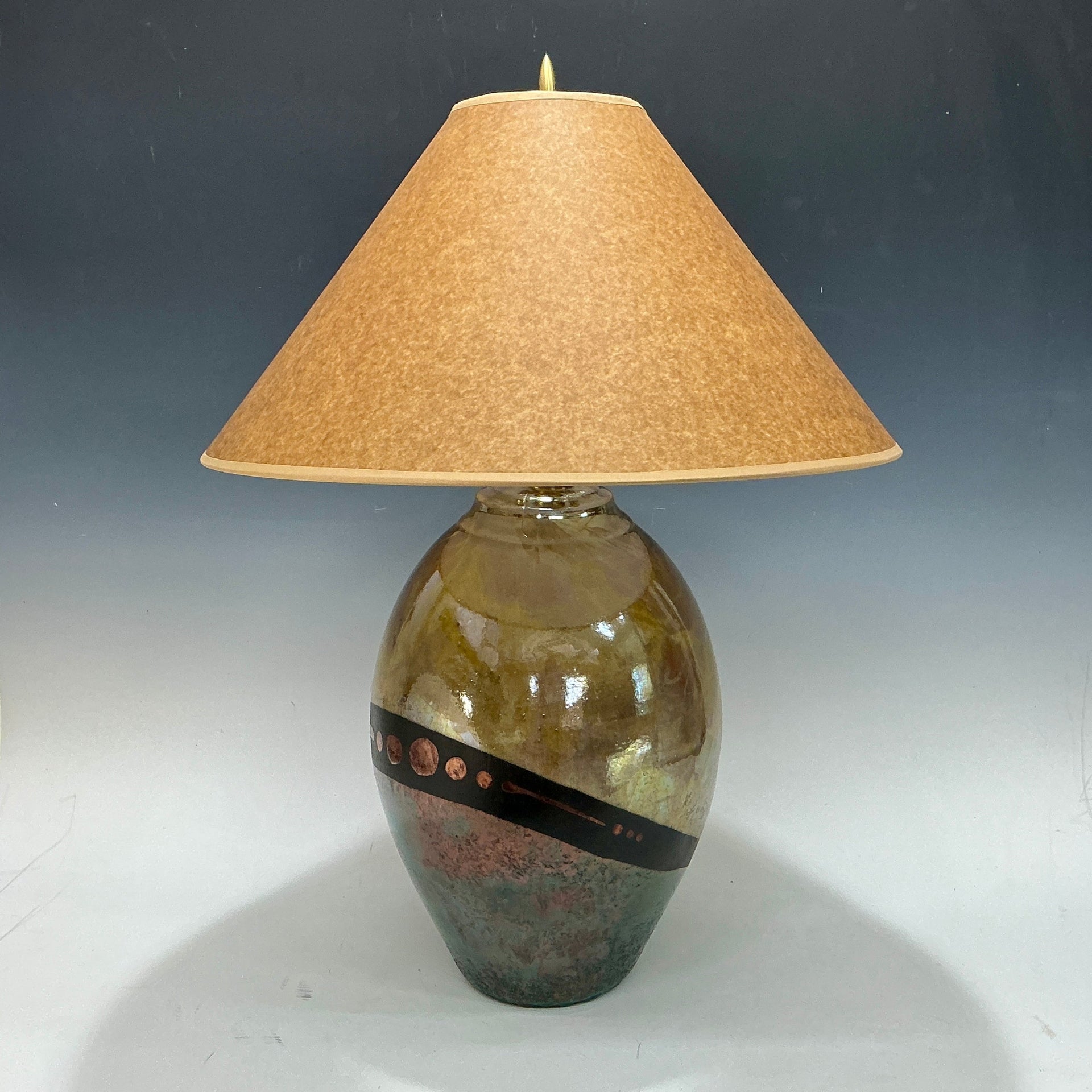 Decorative lamp in gold and teal with a textured shade on a gray background