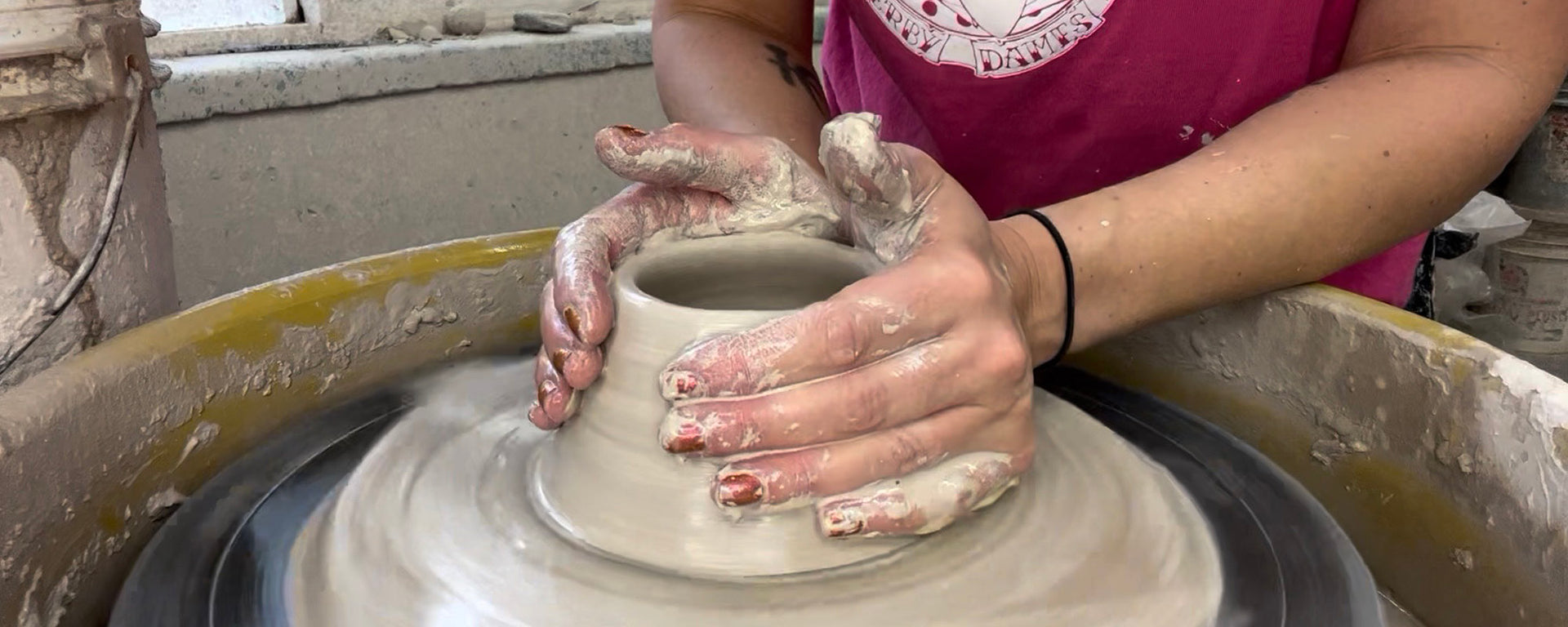 Person making a pot on a pottery wheel with clay in hand