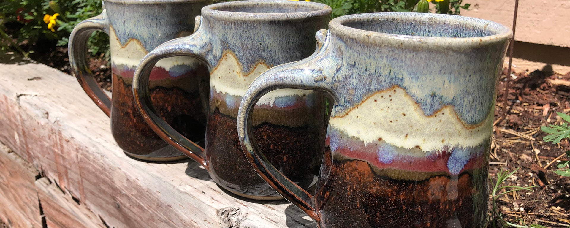 Three ceramic mugs with rustic glaze on a wooden surface outdoors.