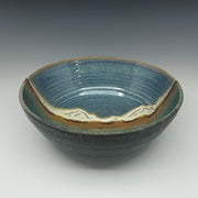 Ceramic bowl with blue glaze and mountain design on a gray background