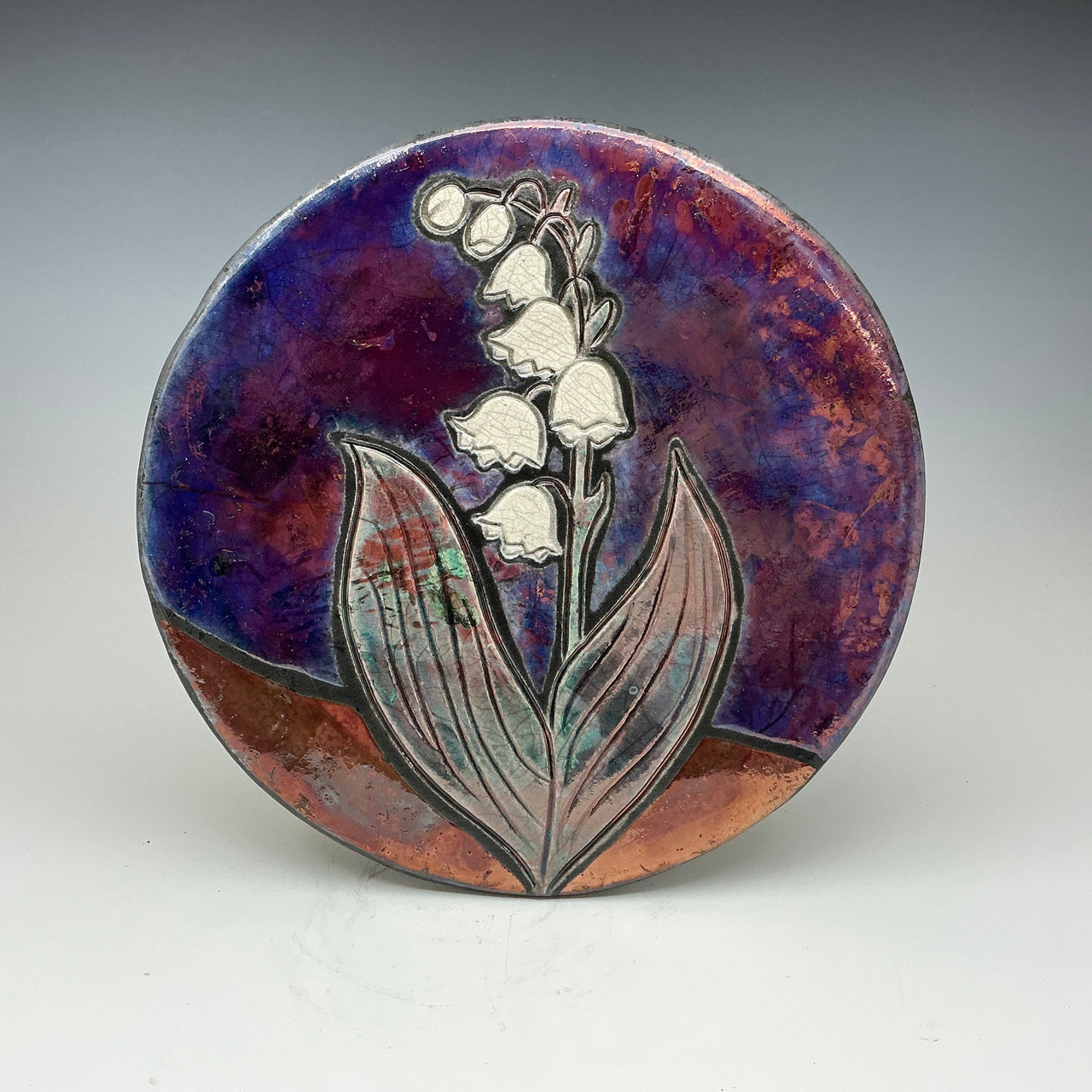 Raku tile with an image of a Lilly of the valley flower on it