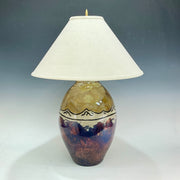 Decorative table lamp with a ceramic base with mountains on it  and white shade on a gray background