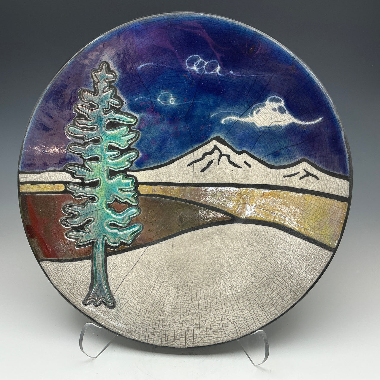 a round pottery plate with an image of mountains and a tree on it