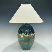 Decorative lamp with a ceramic base with mountains on it and white shade on a dark background