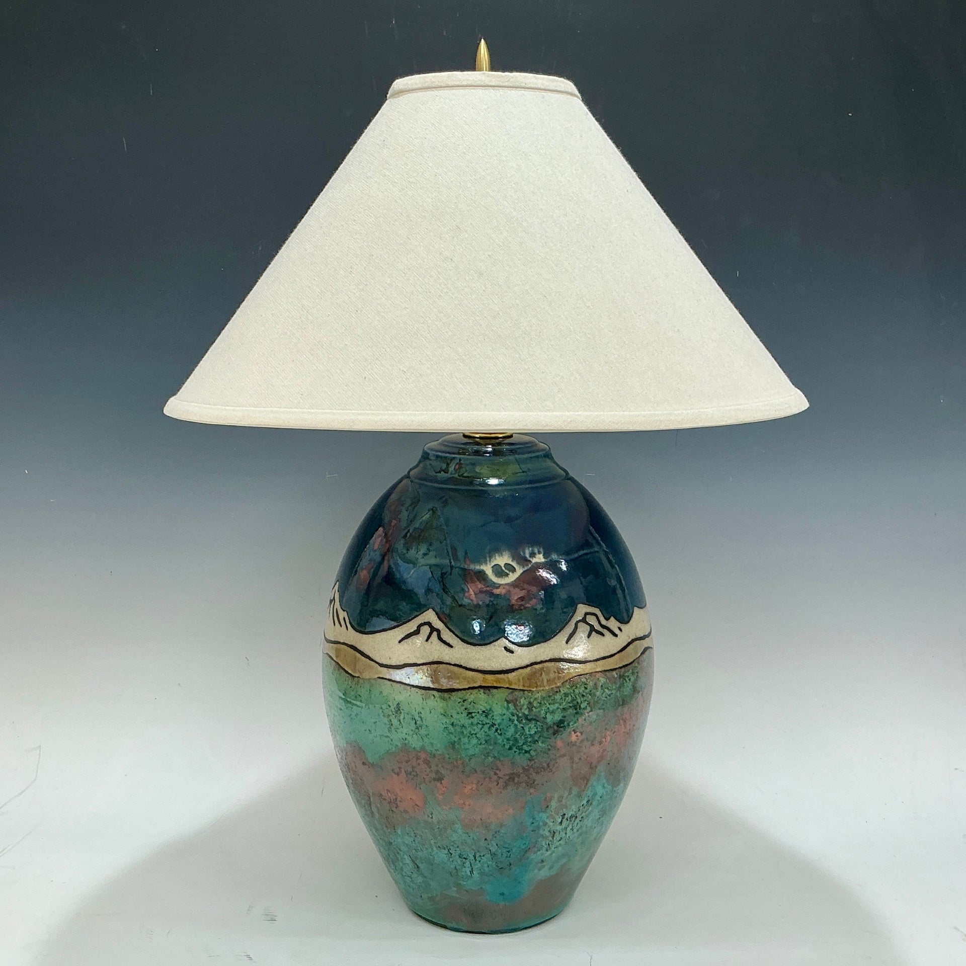 Decorative lamp with a ceramic base with mountains on it and white shade on a dark background