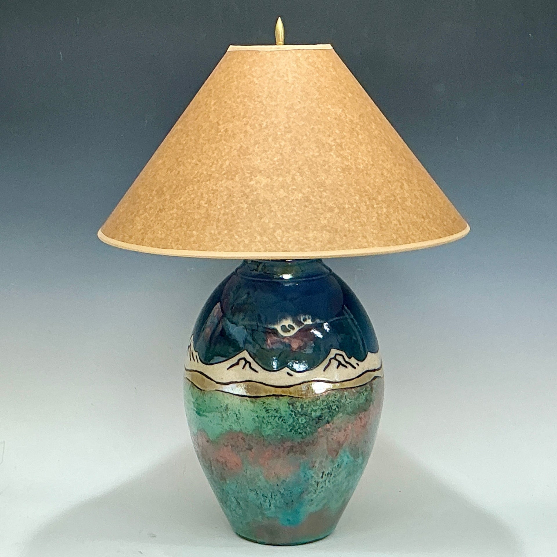 Decorative lamp with a ceramic base with mountains and beige lampshade on a gray background