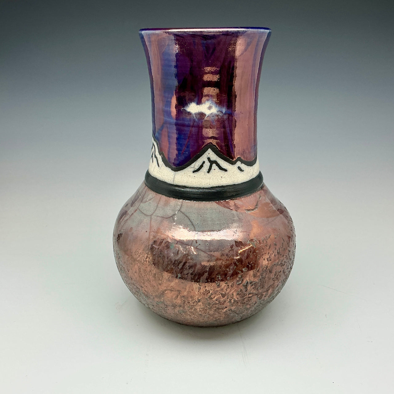 Raku vase with an image of mountains in blue, white teal and copper.