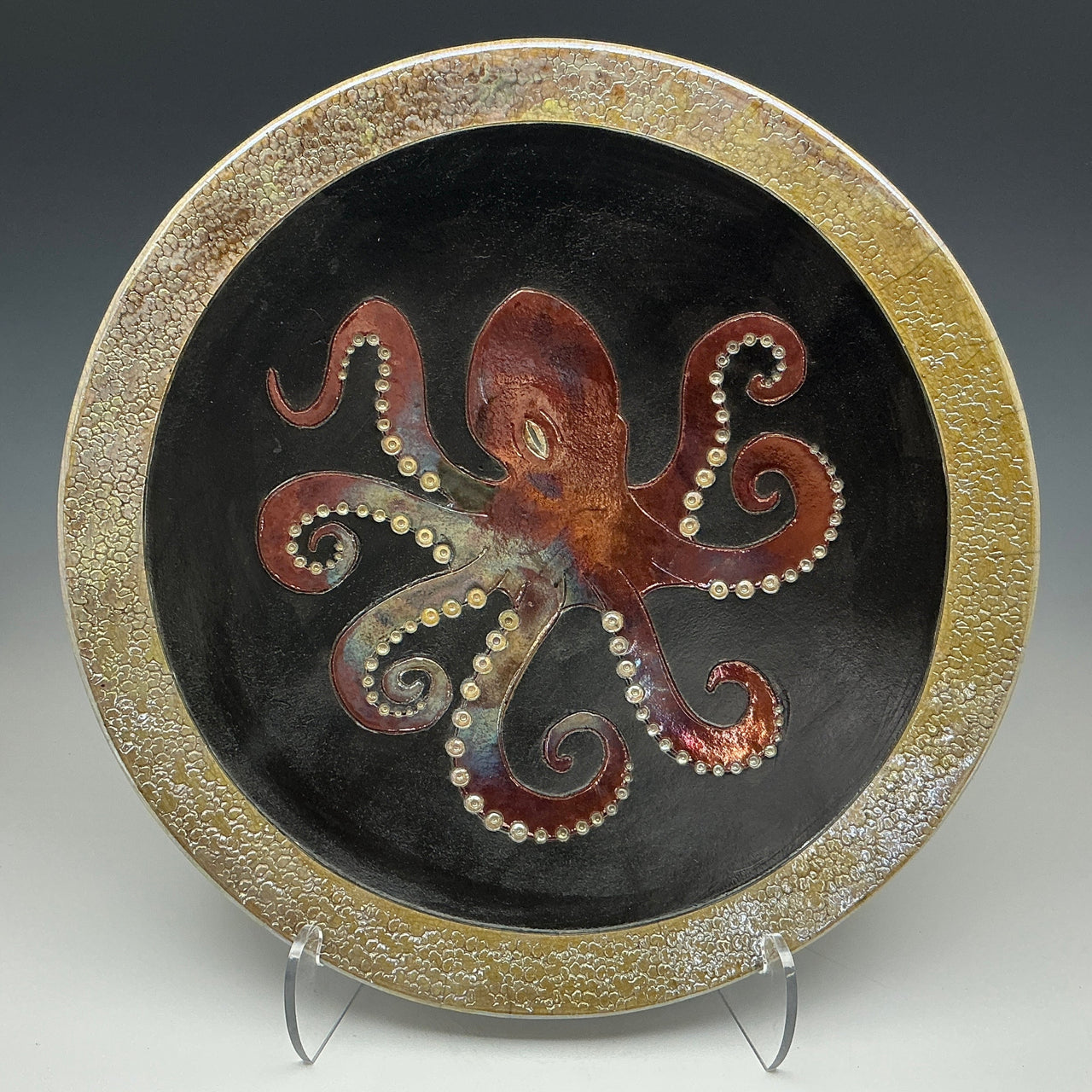raku plate with a giant pacific octopus on a black background and a gold frame.