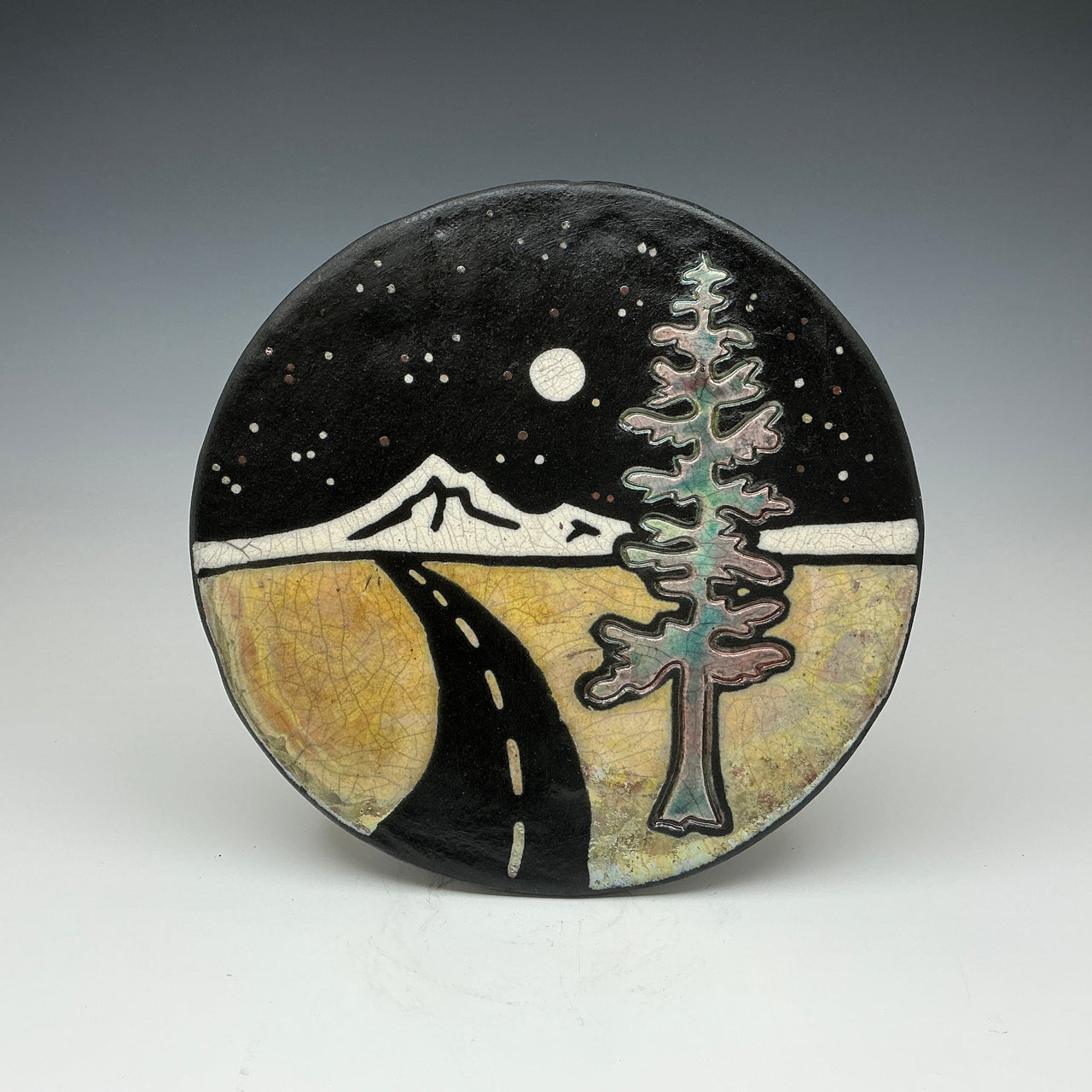 Ceramic plate with a night scene design featuring a tree, mountain, and road.