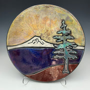 a pottery plate with a golden sky, mountains and a tree on it.