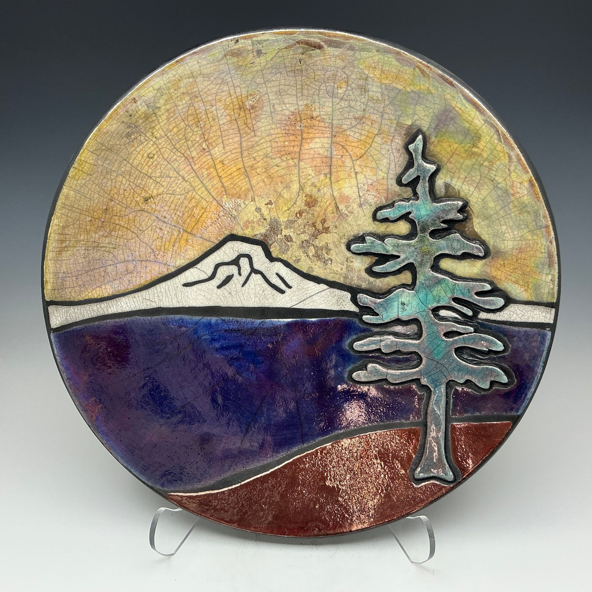 a pottery plate with a golden sky, mountains and a tree on it.